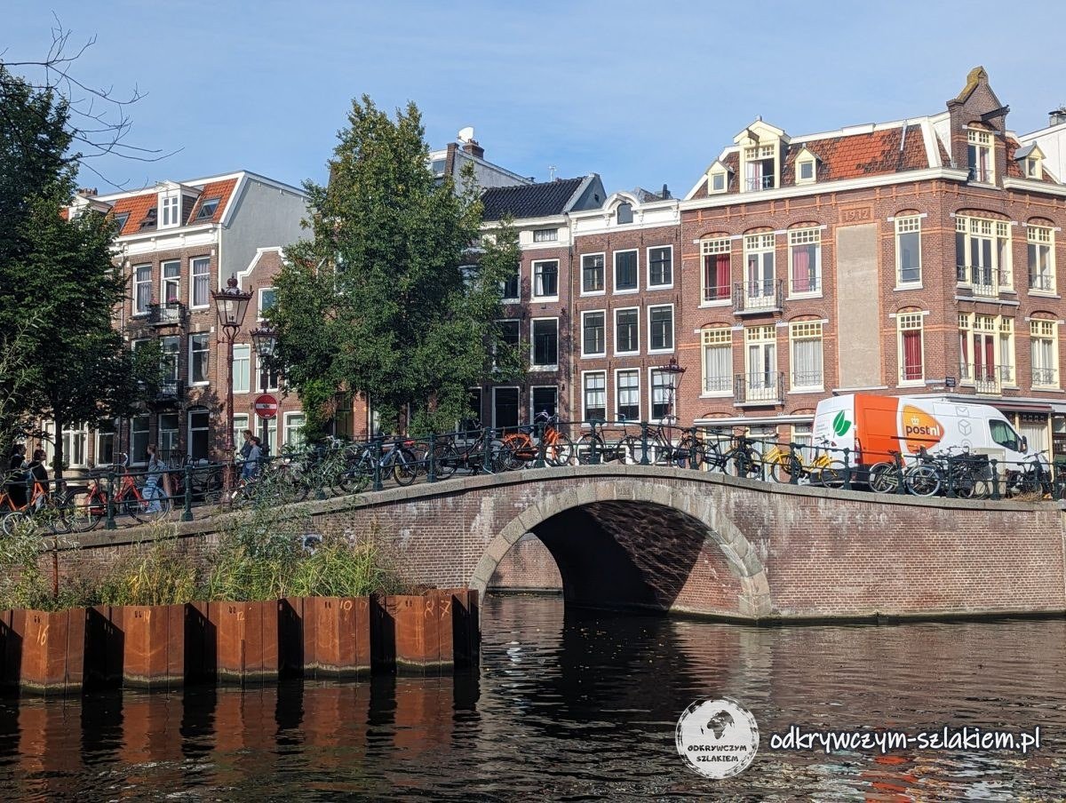 An arched brick bridge over a canal in Amsterdam, with houses and bikes behind