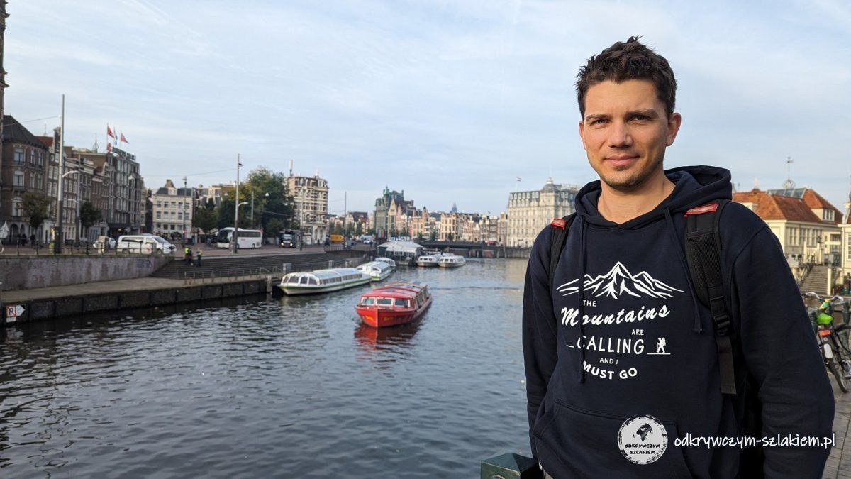 Maciek by the water in front of Centraal station in Amsterdam, with tour boats and houses behind