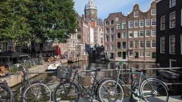 Kanał Oudezijds Voorburgwal w Amsterdamie z rowerami na moście, kamienicami ze szczytami i kopułą bazyliki św. Mikołaja