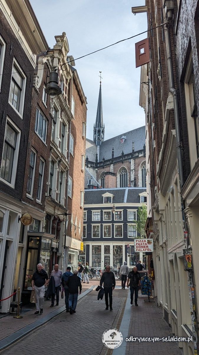 A narrow street with houses in Amsterdam leading to the New Church with its Gothic spire