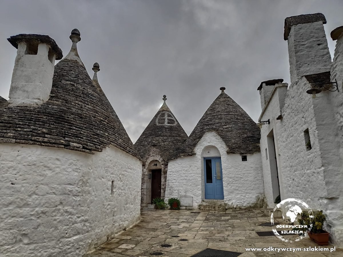 Bielone trulle ze stożkowymi dachami z kamienia na placyku w Alberobello