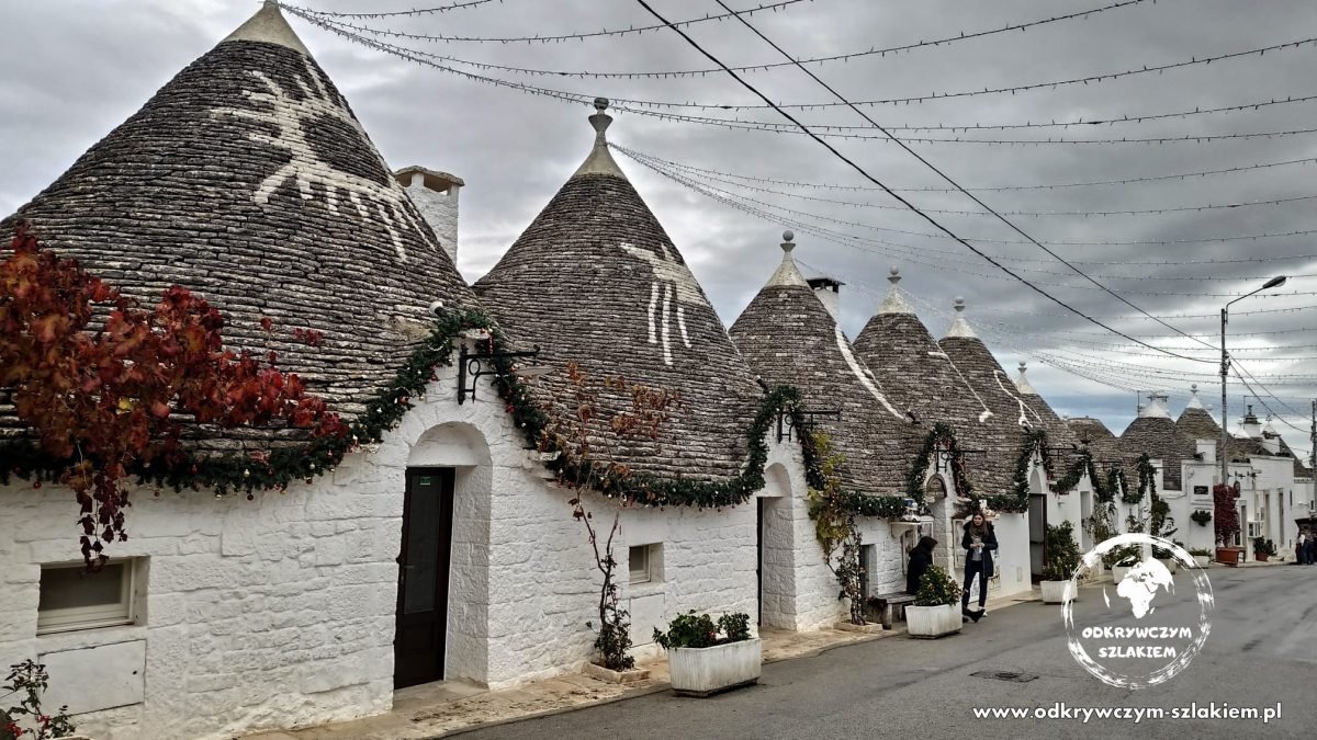 Rząd trulli z białymi symbolami na stożkowych dachach w dzielnicy Rione Monti w Alberobello