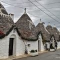 Rząd trulli z białymi symbolami na stożkowych dachach w dzielnicy Rione Monti w Alberobello