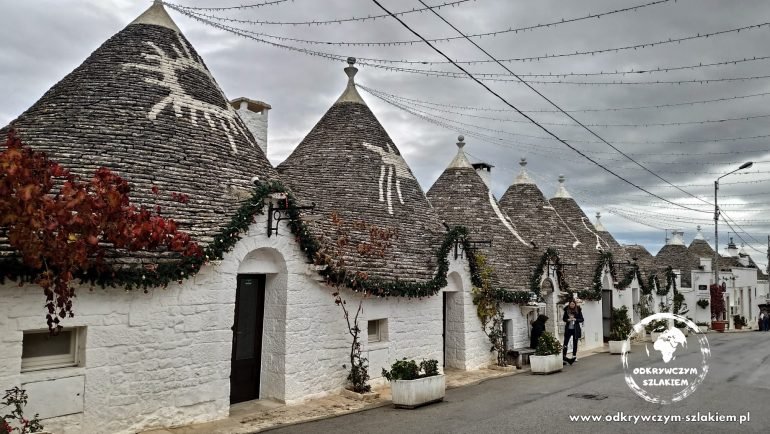 Rząd trulli z białymi symbolami na stożkowych dachach w dzielnicy Rione Monti w Alberobello