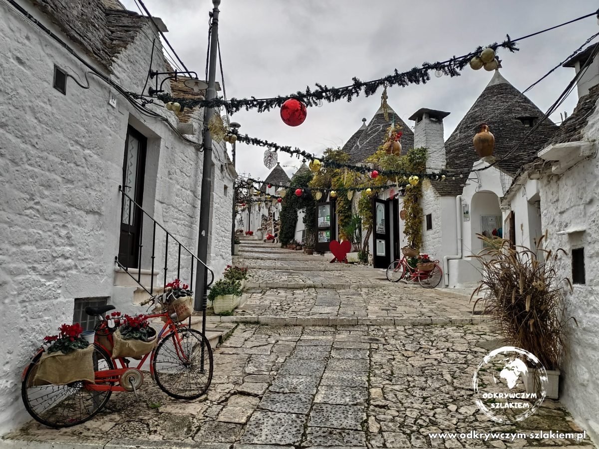 Uliczka między trullami w Alberobello przystrojona na święta, z czerwonym rowerem z kwiatami