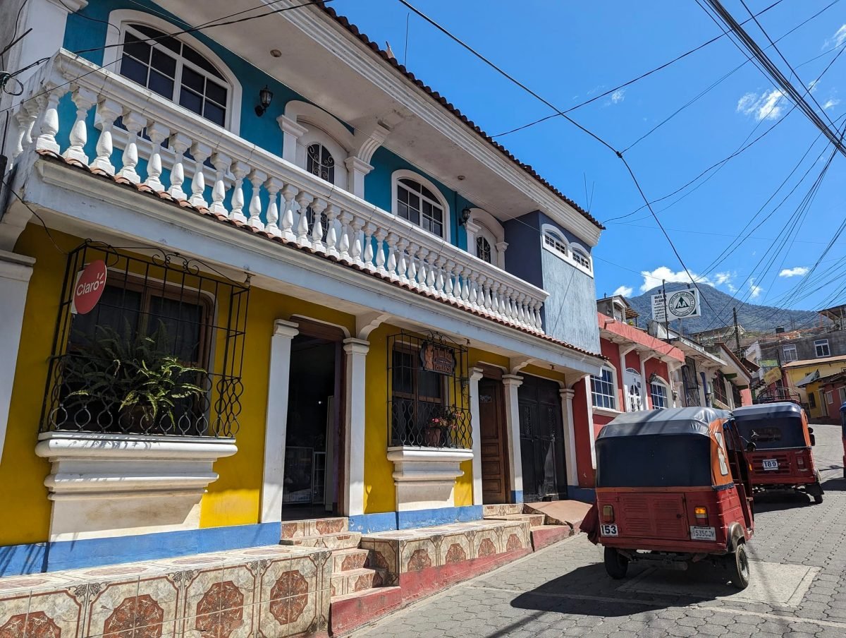 Kolorowy dom i tuk-tuki na ulicy San Juan La Laguna, w tle wulkan