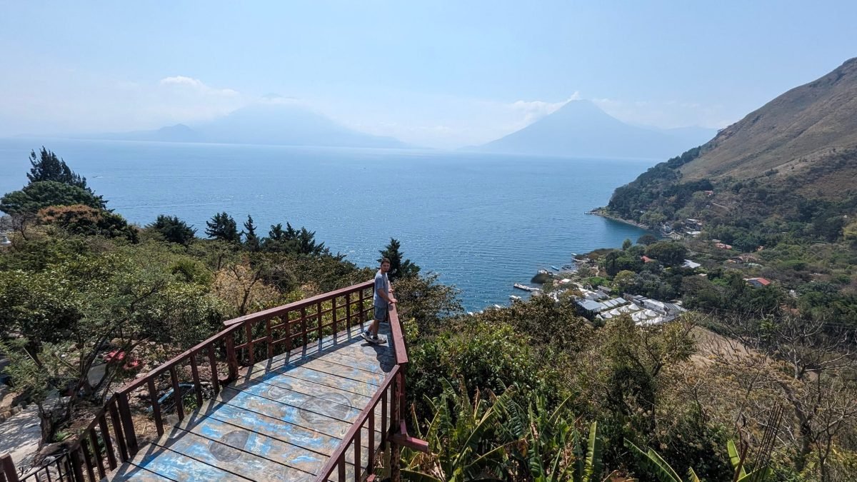 Drewniany taras widokowy Mirador Tzanjuyú nad jeziorem Atitlán, w dole brzeg Santa Cruz La Laguna, w oddali wulkany we mgle