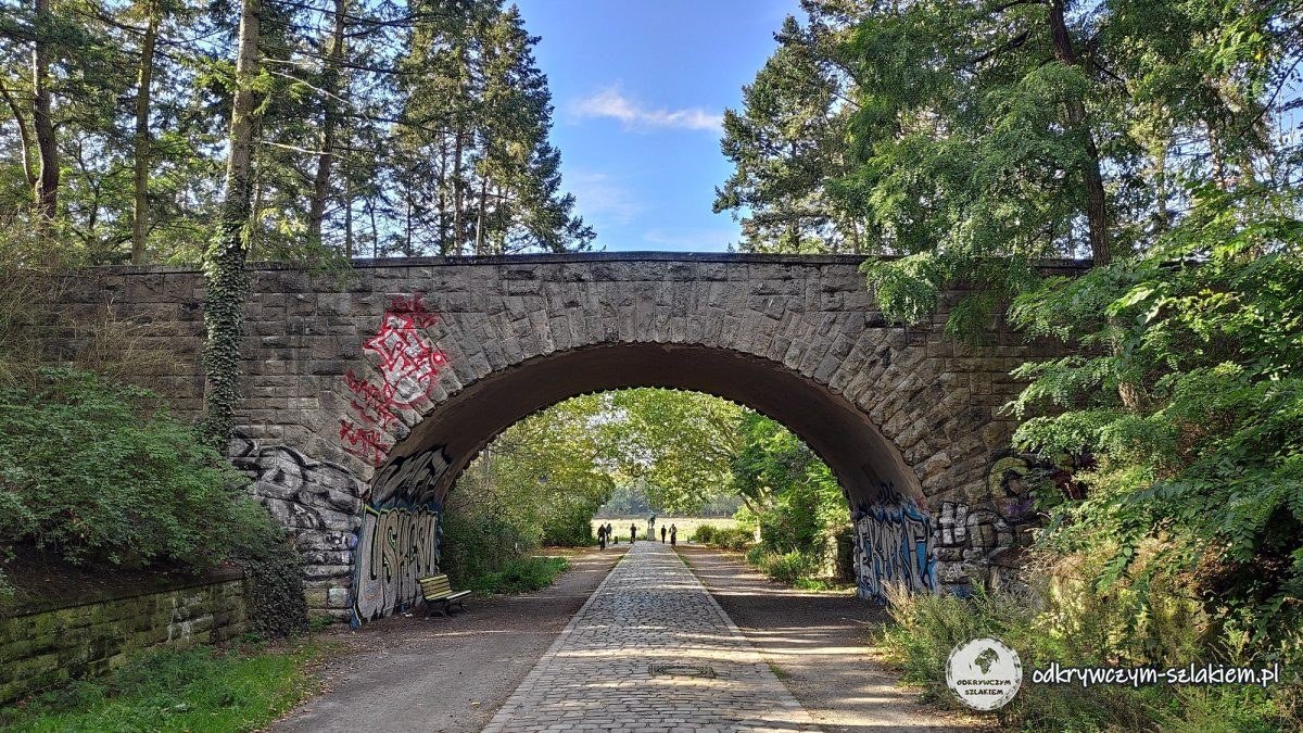Eine steinverkleidete Bogenbrücke über einem Weg im Volkspark Rehberge