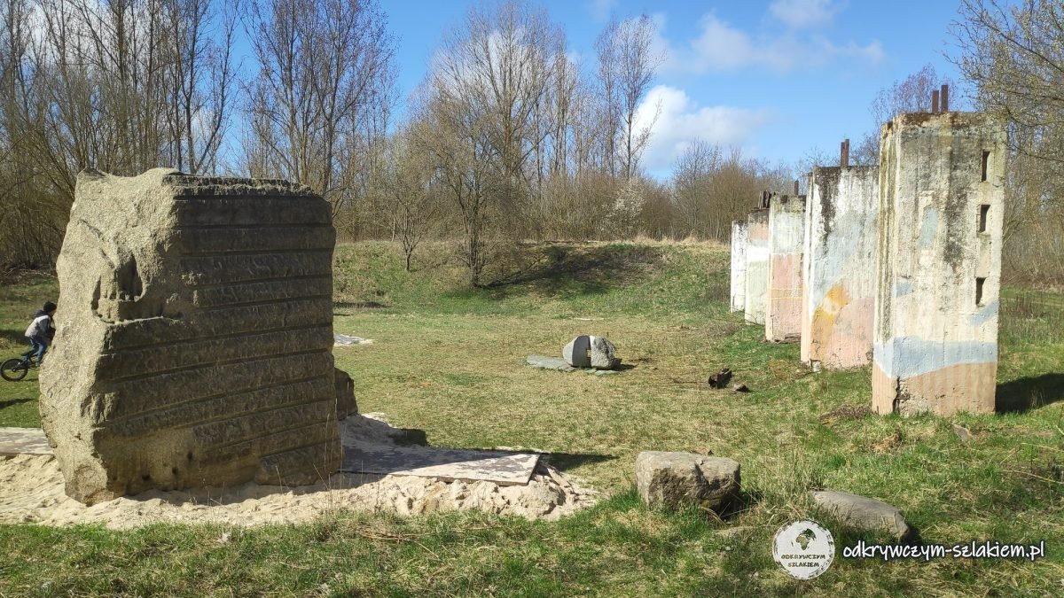 Rząd kolorowo pomalowanych słupów dawnej stodoły majątku Hobrechtsfelde wśród drzew
