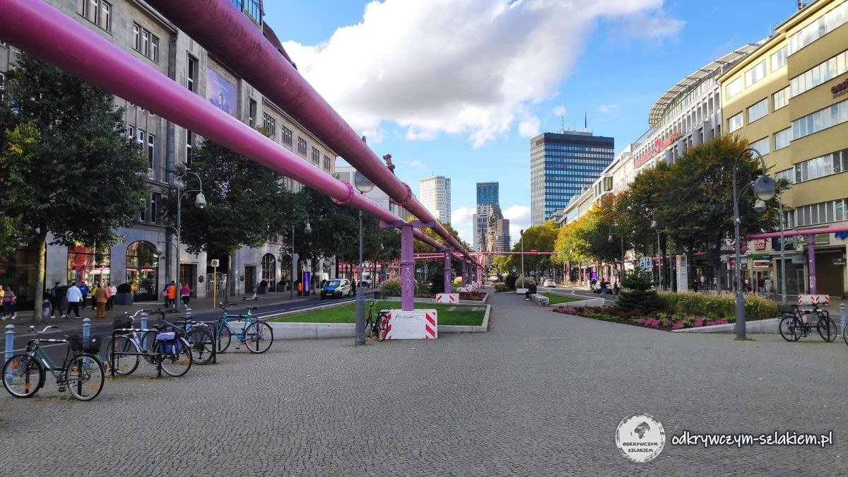 La Tauentzienstraße con tuberías rosas sobre la franja verde y, al fondo, la torre de la Iglesia Memorial