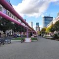 Tauentzienstraße z różowymi rurami nad pasem zieleni, w głębi wieża Kościoła Pamięci