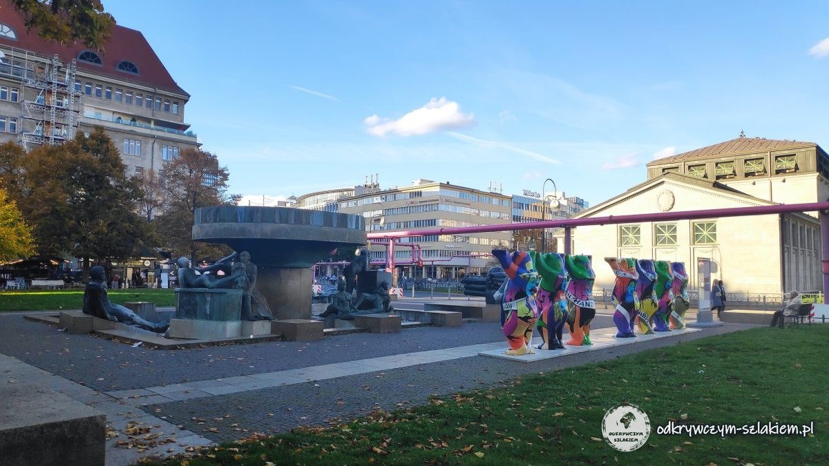Fuente con esculturas de figuras recostadas y Buddy Bären delante del pabellón del metro en la Wittenbergplatz