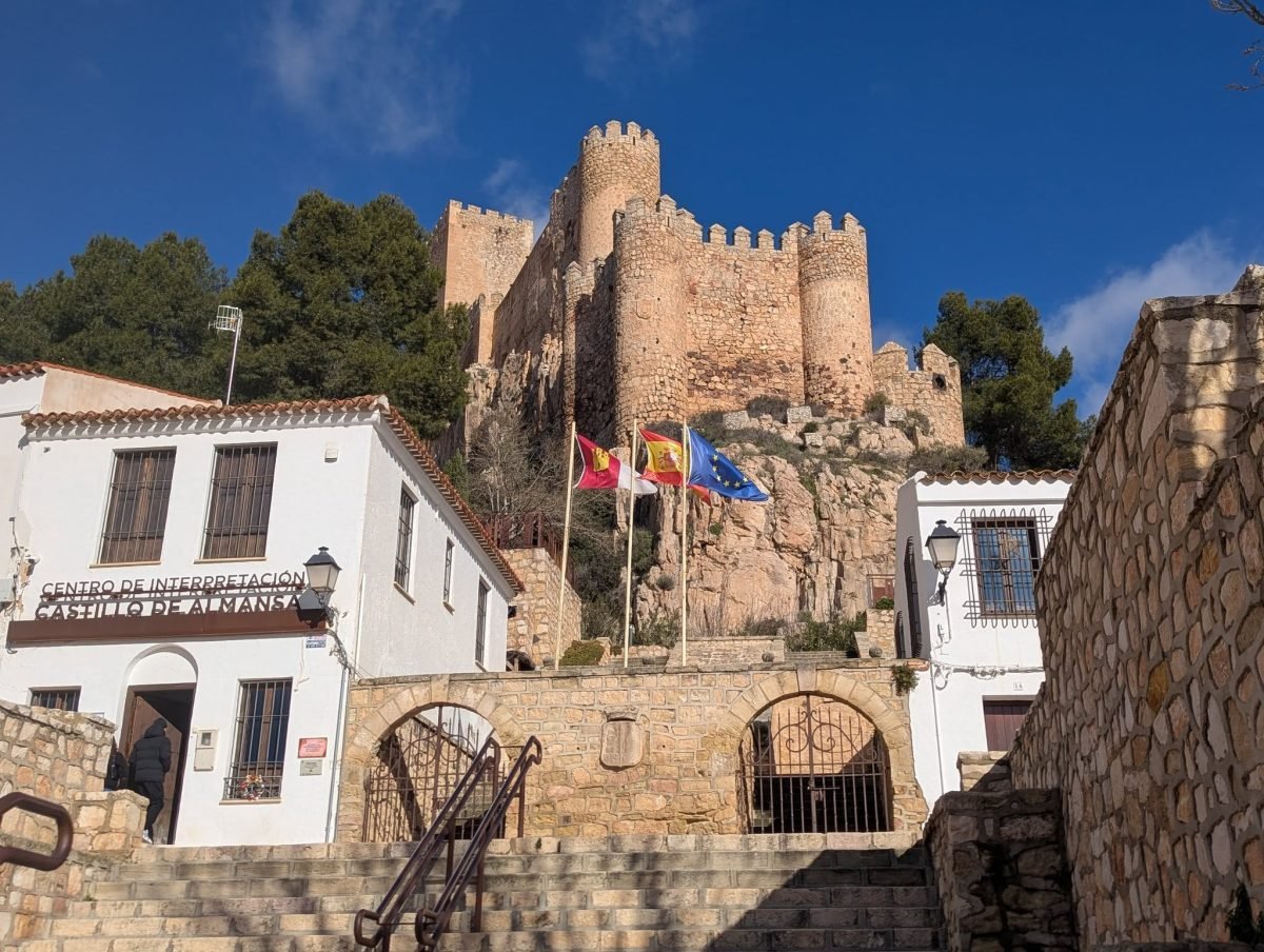Zamek w Almansie na skale nad schodami i centrum informacyjnym Castillo de Almansa, z flagami Kastylii-La Manchy, Hiszpanii i Unii Europejskiej