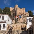 Zamek w Almansie na skale nad schodami i centrum informacyjnym Castillo de Almansa, z flagami Kastylii-La Manchy, Hiszpanii i Unii Europejskiej