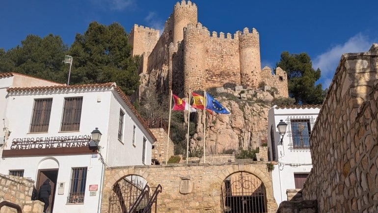 Zamek w Almansie na skale nad schodami i centrum informacyjnym Castillo de Almansa, z flagami Kastylii-La Manchy, Hiszpanii i Unii Europejskiej
