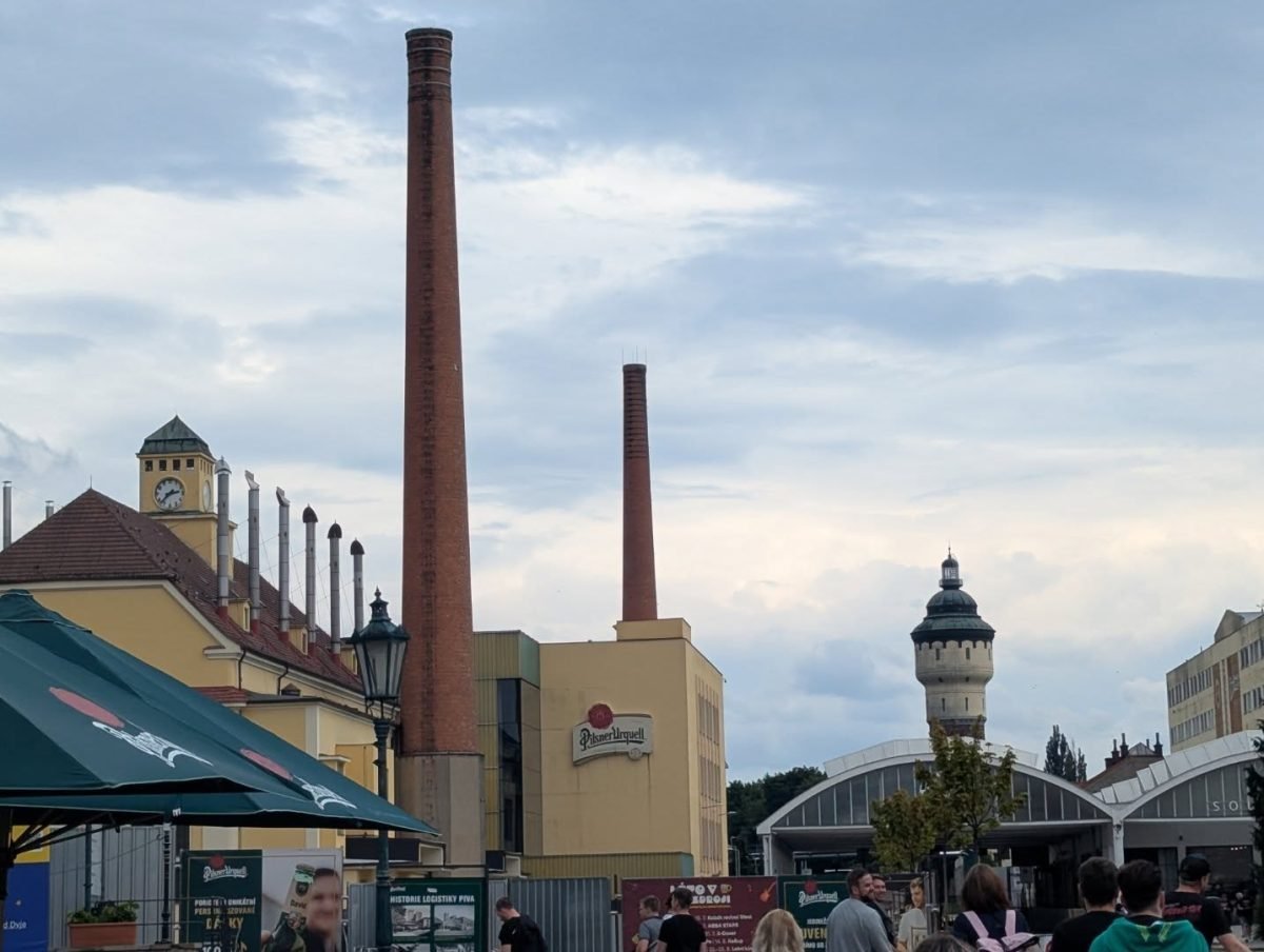 Teren browaru Pilsner Urquell w Pilźnie z wysokimi kominami i wieżą ciśnień