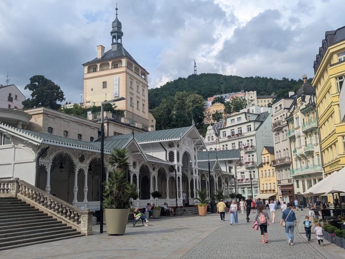 Biała, drewniana Kolumnada Rynkowa i wieża zamkowa nad deptakiem w Karlowych Warach