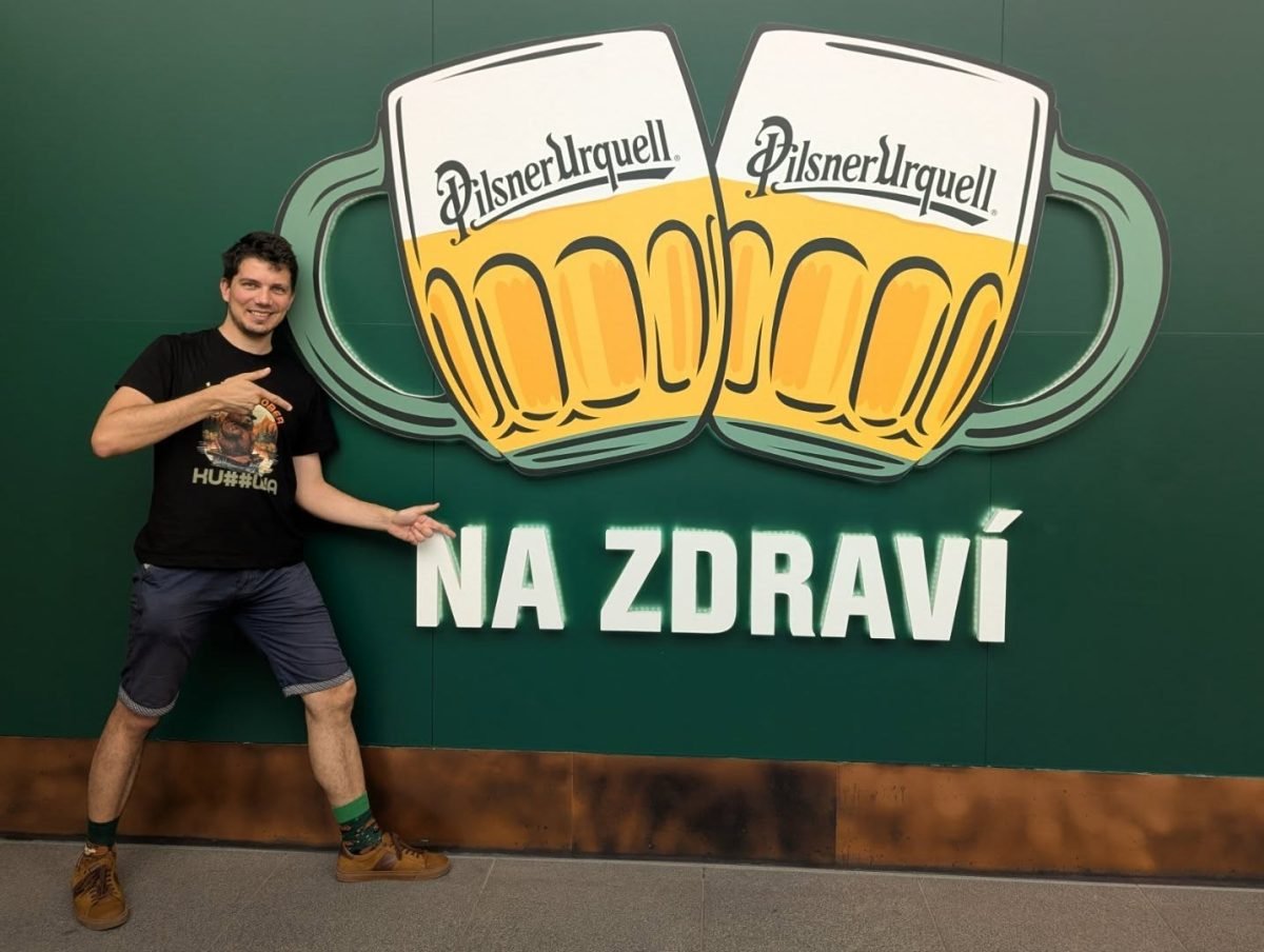 Pozowanie przy ścianie z kuflami Pilsner Urquell i napisem Na zdraví w browarze w Pilźnie