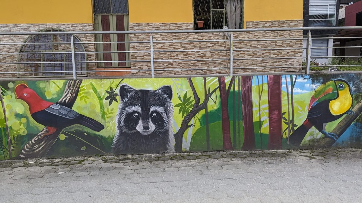 Mural z tukanem, szopem i ptakami w dżungli na murze przy ulicy w Baños