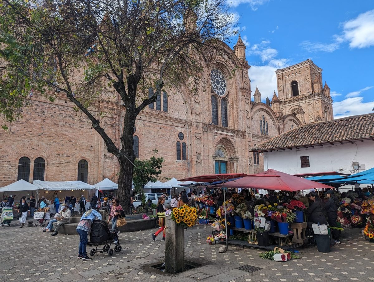Stragany z kwiatami pod czerwonymi parasolami przy ceglanej katedrze w Cuenca