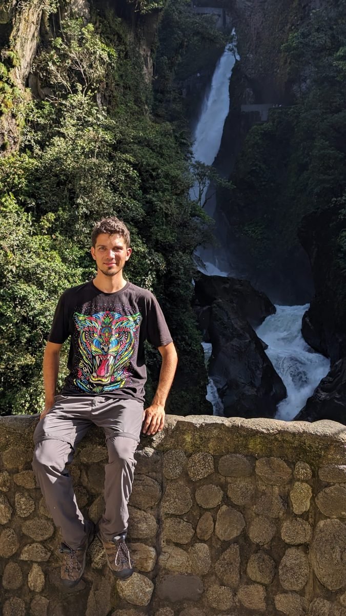 Maciek siedzi na kamiennym murku, za nim wodospad Pailón del Diablo