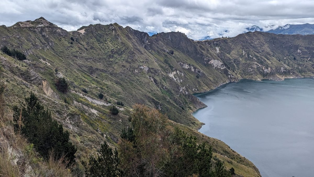 Laguna Quilotoa w kraterze wulkanu widziana z krawędzi, ze stromymi zboczami porośniętymi krzewami