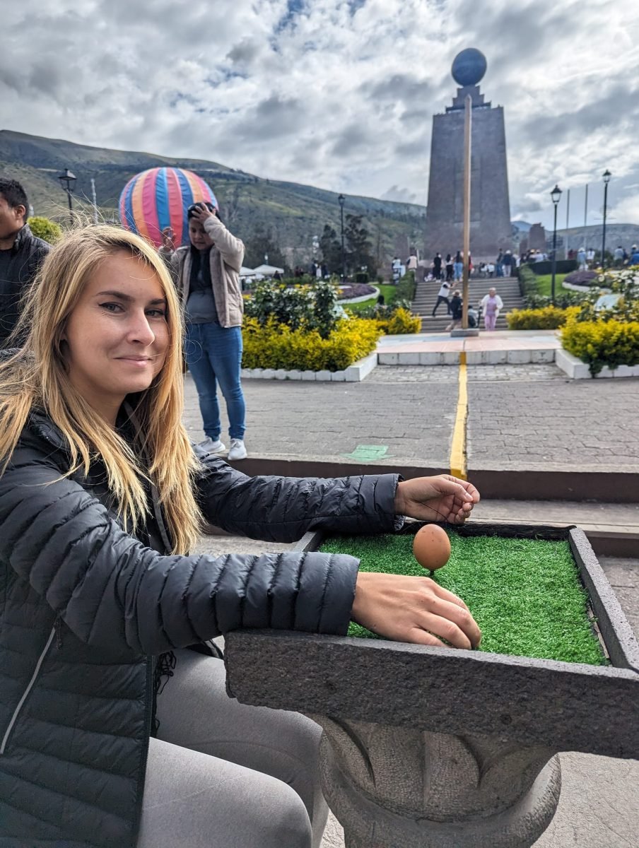 Patrycja próbuje ustawić jajko na główce gwoździa w Mitad del Mundo, w tle pomnik z kulą