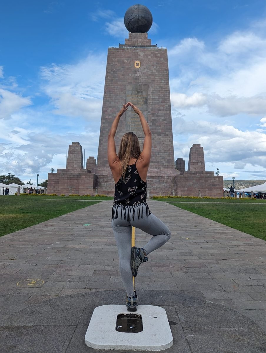 Patrycja w pozycji drzewa na linii równika przed pomnikiem z kulą ziemską w Mitad del Mundo