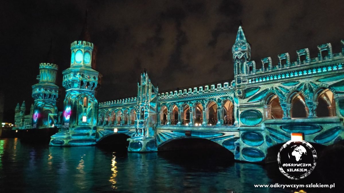 Most Oberbaumbrücke nad Szprewą w turkusowej projekcji odbitej w wodzie (Festival of Lights 2021)