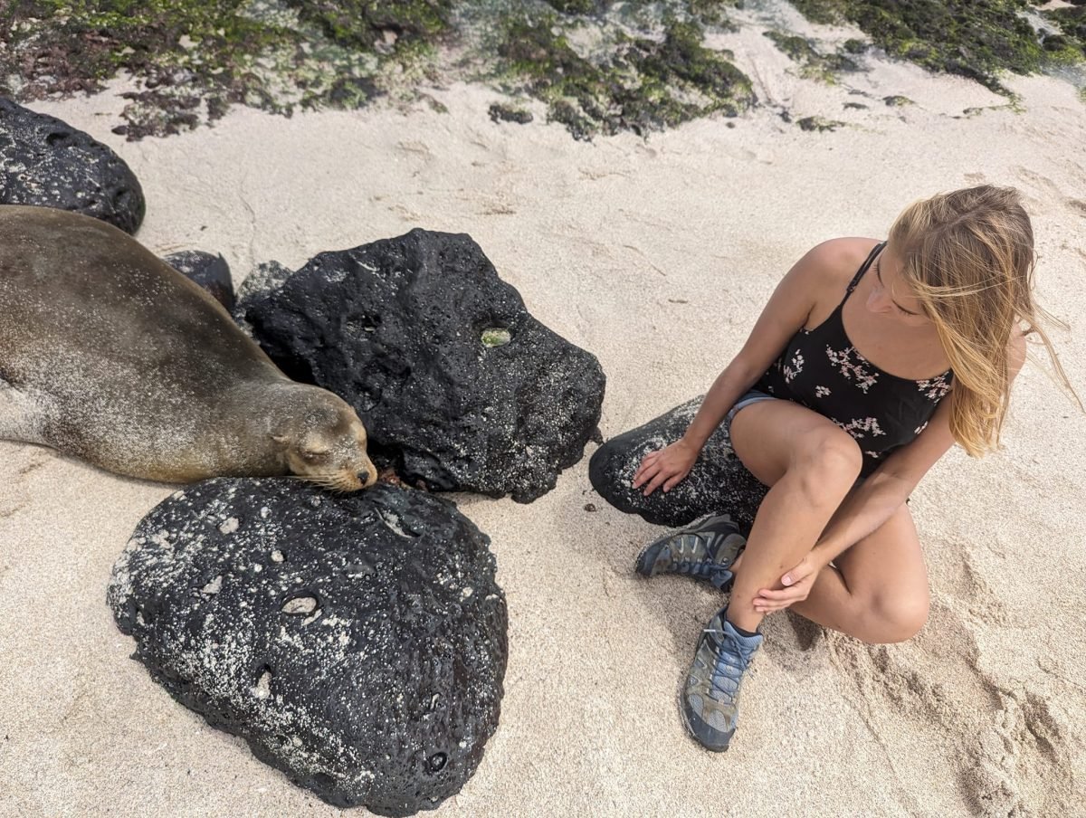 Patrycja siedzi na plaży obok śpiącego lwa morskiego na San Cristóbal