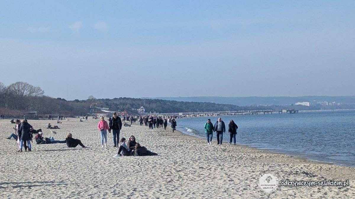 Spaziergänger am breiten Strand von Brösen an einem sonnigen Märztag, in der Ferne die Seebrücke