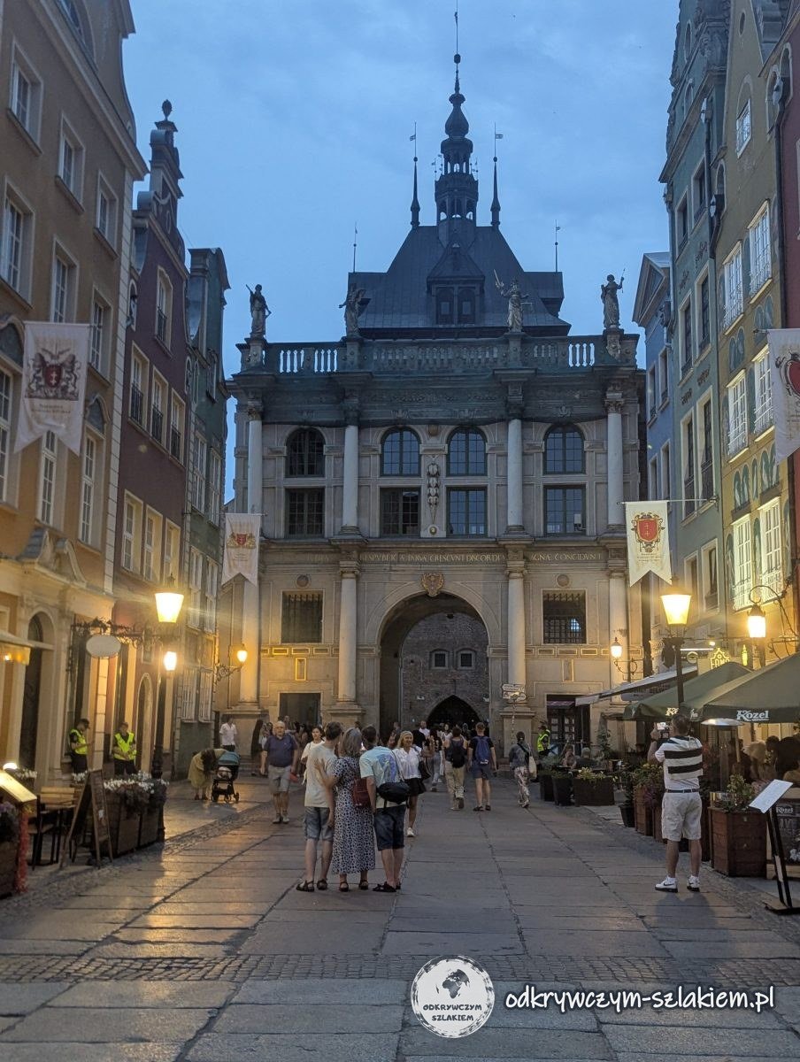 The Golden Gate at the end of Long Street in Gdańsk in the evening, with lit street lamps and people strolling