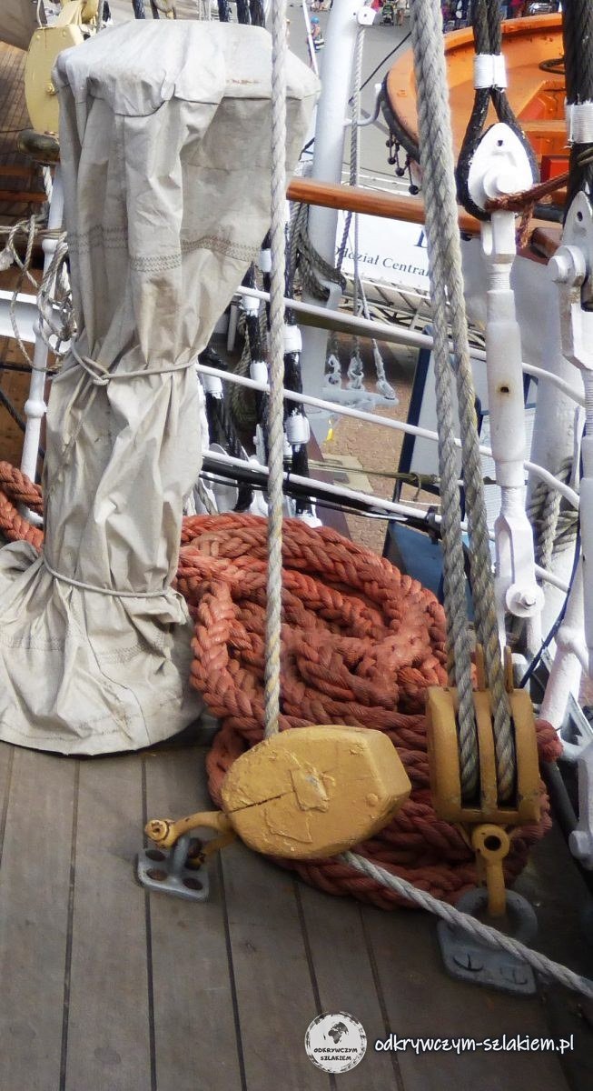 A coil of rope, a yellow block and shrouds on the wooden deck of Dar Pomorza, with the quay behind