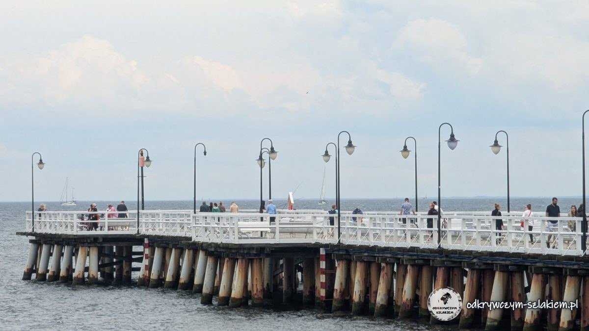 The wooden pier in Orłowo with white railings and lamps, people strolling on the deck