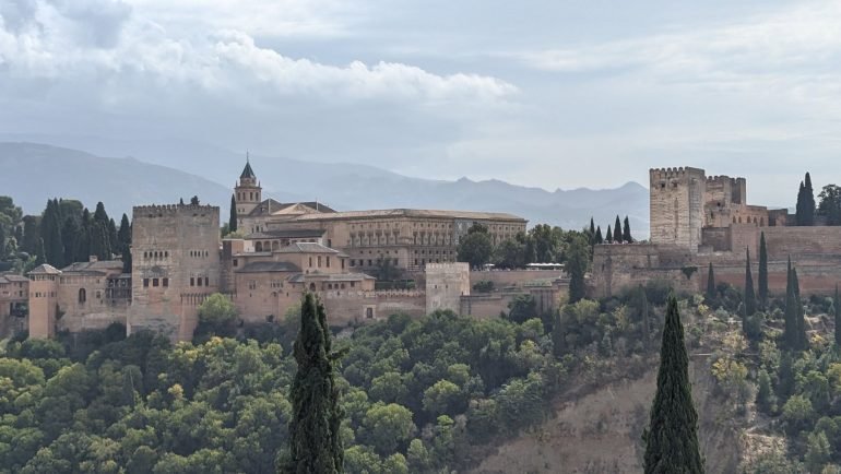 Alhambra na wzgórzu nad Grenadą, z cyprysami na pierwszym planie i pasmem Sierra Nevada w tle