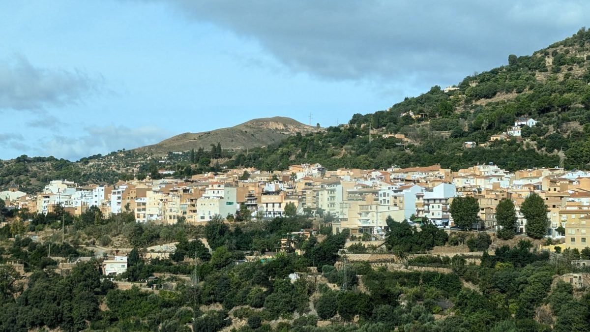 Białe miasteczko na zboczu porośniętym drzewami w regionie Alpujarras w górach Sierra Nevada