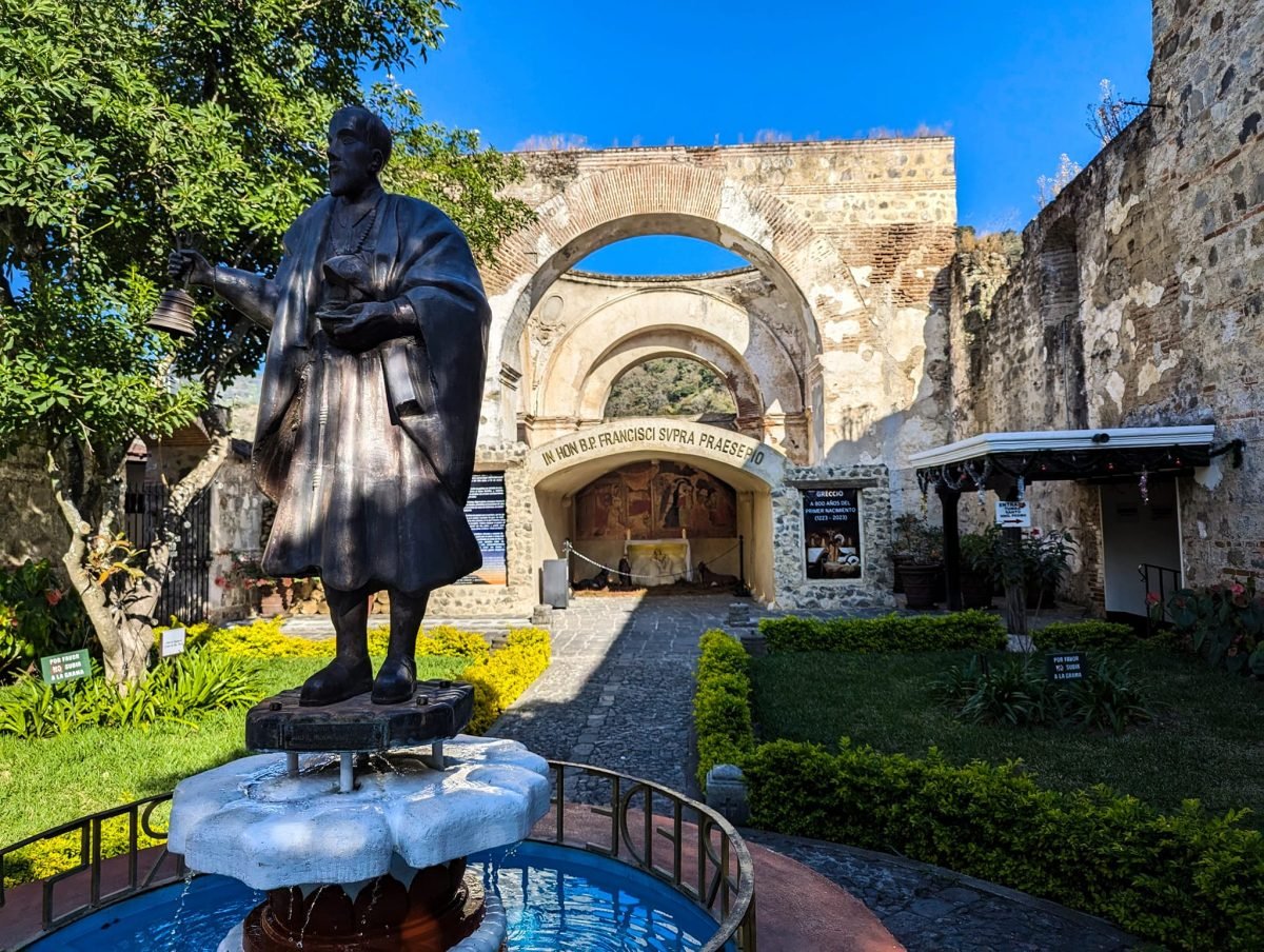 Figura zakonnika w ogrodzie przed ruinami łukowych arkad kościoła w Antigua Guatemala