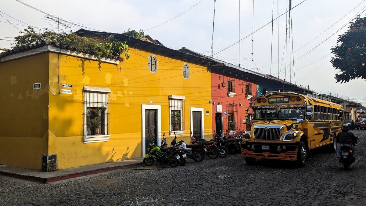 Niski, żółty kolonialny dom na rogu ulicy i przejeżdżający chicken bus w Antigua Guatemala