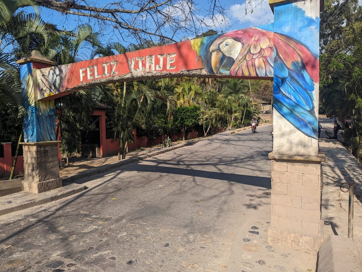 Brama z napisem Feliz viaje i malowaną arą nad ulicą w Copán Ruinas