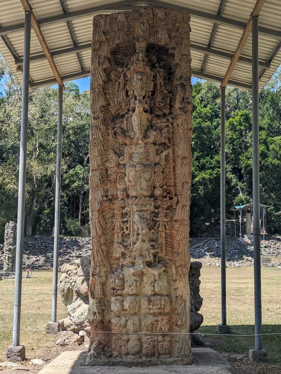 Wysoka stela władcy pod zadaszeniem na placu w ruinach Copán