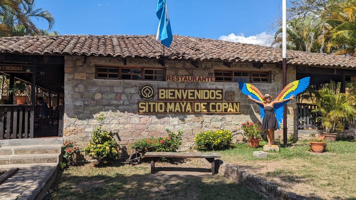 Patrycja ze skrzydłami ary przy napisie Bienvenidos Sitio Maya de Copán przy wejściu do ruin
