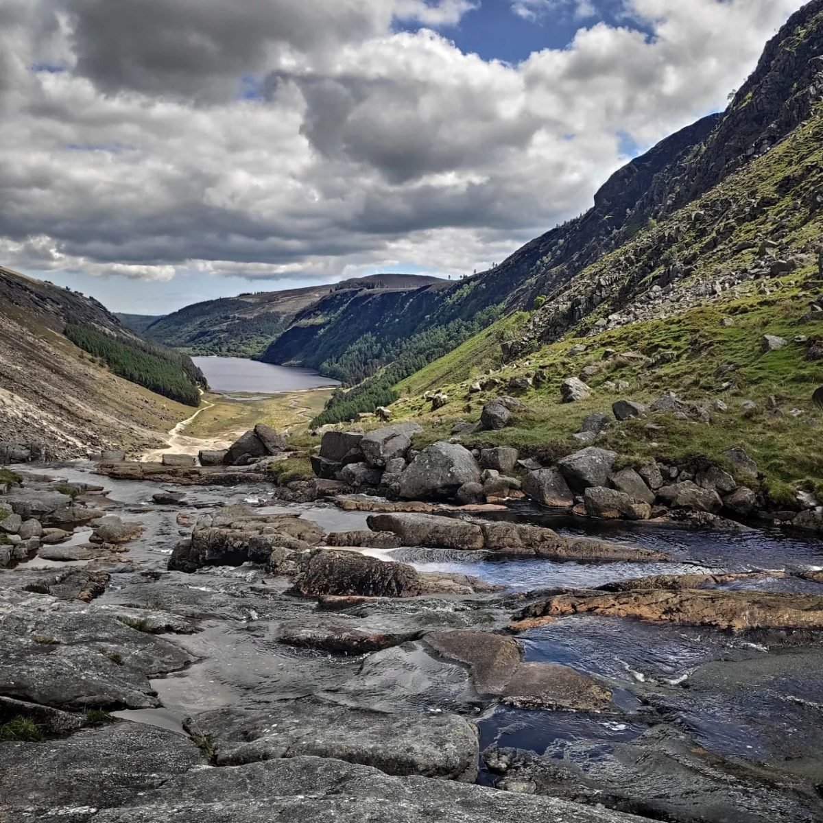 Kaskady górskiej rzeki wśród skał, w głębi doliny jezioro Upper Lake w Glendalough