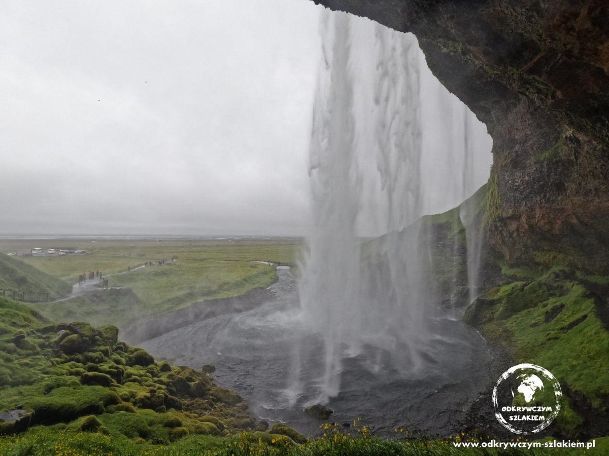 Widok zza wodospadu Seljalandsfoss na zieloną równinę
