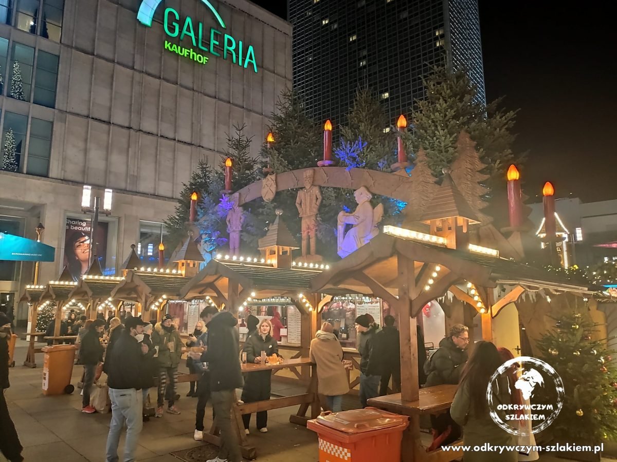 Ławy i budki z jedzeniem na jarmarku przy Alexanderplatz pod domem towarowym Galeria