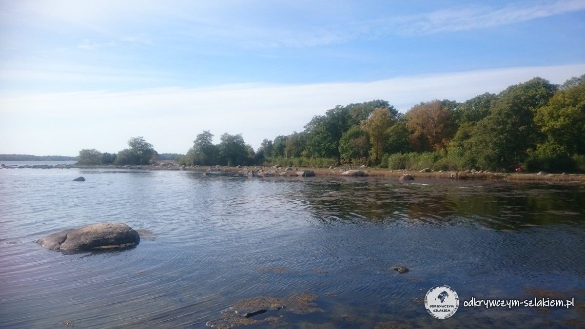 El agua tranquila de una bahía con una roca junto a la orilla y árboles otoñales en la reserva natural de Almö