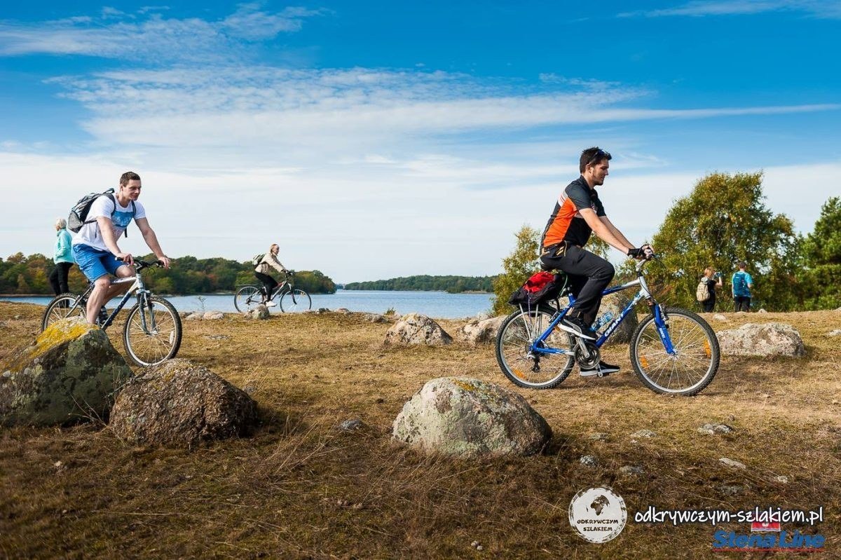 Dos ciclistas sobre la hierba seca entre rocas junto a una bahía cerca de Karlskrona