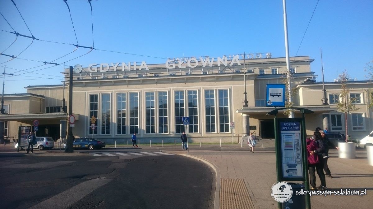El edificio de la estación Gdynia Główna, con grandes ventanales y un rótulo en el tejado, al sol de la mañana