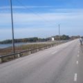 Una carretera asfaltada por un terraplén sobre el agua camino de la isla de Hasslö, con un ciclista a lo lejos y una señal de 70 km/h