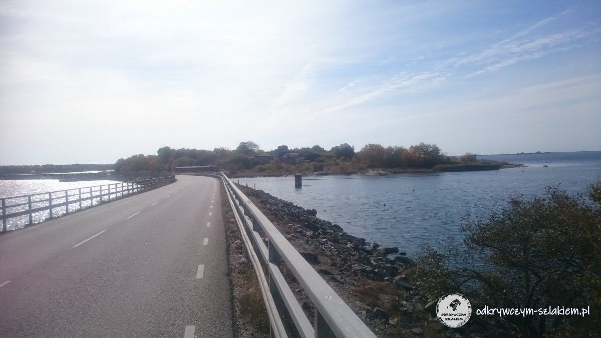 Una carretera con barandillas por un terraplén hacia un islote con fortificaciones de hormigón, cerca del puente de Hasslö
