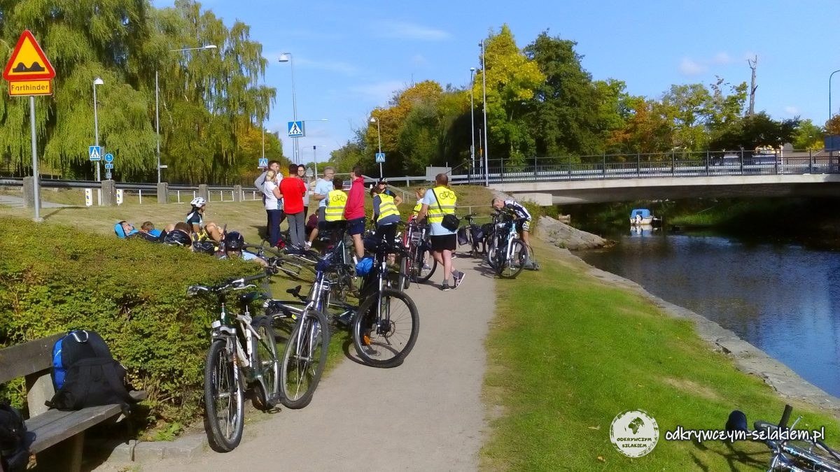 Un grupo de ciclistas y guías con chalecos amarillos descansando junto al río Nättrabyån, al lado del puente de Nättraby